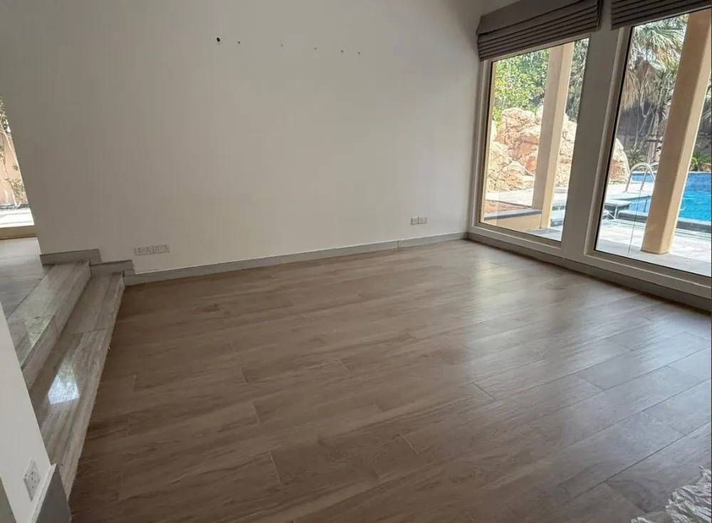 Before: empty family room with wood-look floor and windows to the pool